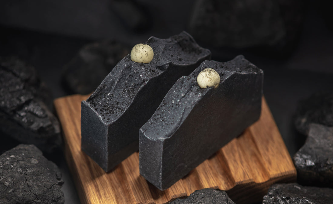 Natural black charcoal soap in a wooden soap dish surrounded by coals concept of making and using organic soap and cosmetics eco handmade presents