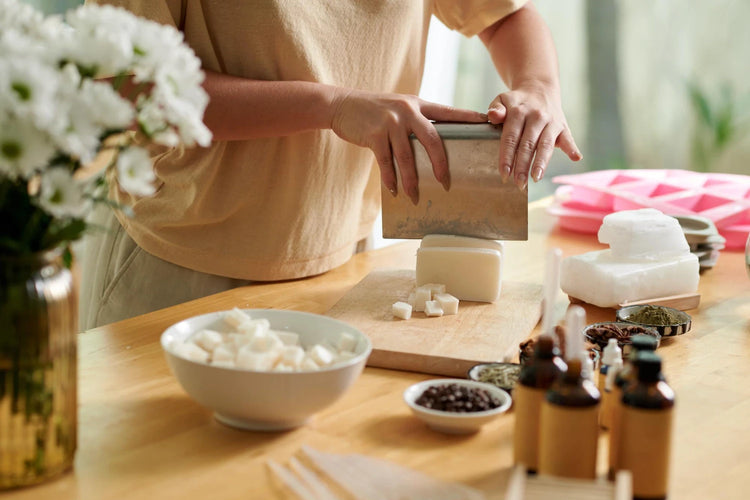 Person preparing ingredients on a wooden table with flowers and bottles in the background